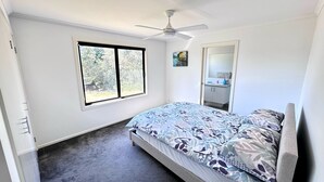 A bedroom with a bed, a ceiling fan, a window, and a bathroom visible through an open door. - Escape to Henry's Inlet Views, a picturesque holiday rental in the charming town of Venus Bay (Venus Bay)