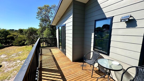 A wooden deck with a glass balustrade, a table, and two chairs. - Escape to Henry's Inlet Views, a picturesque holiday rental in the charming town of Venus Bay (Venus Bay)