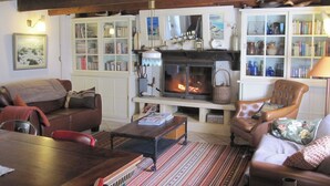 Ein gemütliches Wohnzimmer mit Kamin, Holzbalken, einer Couch, Sesseln und eingebauten Bücherregalen.