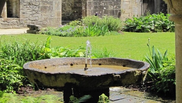 Ein Steinhaus mit Bogenfenstern und einem Brunnen im Vordergrund.