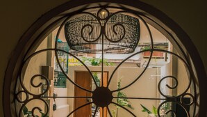 A circular window with intricate metalwork, offering a view of a courtyard with a wooden door, potted plants, and a brick pathway. - Brenda Home (Nha Trang)