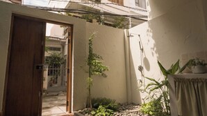 A small courtyard with a wooden door, a small garden with pebbles and plants, and a table with a plant on it. - Brenda Home (Nha Trang)