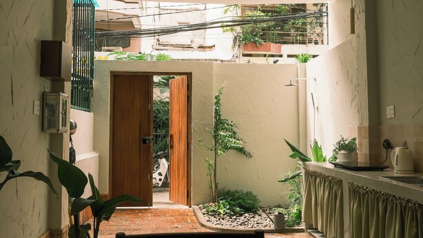 A room with a wooden door leading to a courtyard, a small table, and a chair. - Brenda Home (Nha Trang)