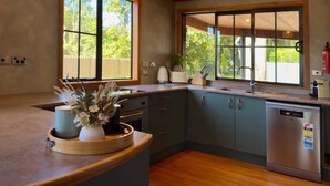 Una cocina moderna con armarios de madera, un lavavajillas de acero inoxidable y ventanas amplias que ofrecen vistas al exterior.