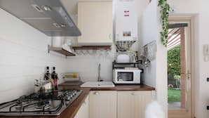 Una cocina con estufa a gas, microondas, lavamanos y vistas al jardín a través de una puerta abierta.