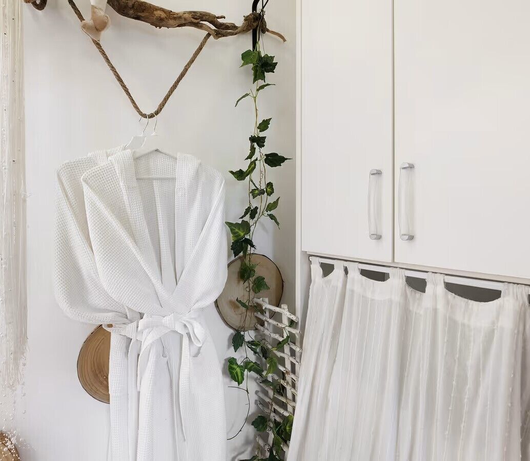 A white wardrobe with two doors, a white robe hanging on a hook, and a white curtain.