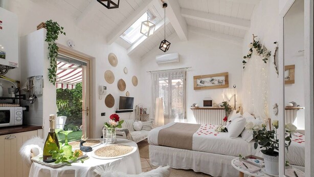 Una habitación luminosa con una cama, una mesa de comedor con una botella y una zona de cocina.