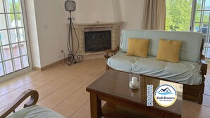 A living room with a sofa, a table, a fireplace, and a fan. - ID #14 BnB Homes Villa (Albufeira)