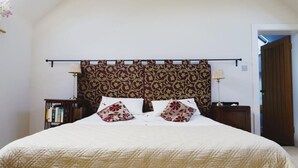 A neatly made bed with a patterned headboard, two bedside tables with lamps, and a bookshelf in a room with white walls and a sloped ceiling. - North Cottage at Boath Stables – A Cozy Highland Escape (Nairn)