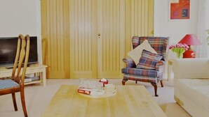 A living room with a wooden coffee table, a plaid armchair, a television on a stand, and a yellow door. - North Cottage at Boath Stables – A Cozy Highland Escape (Nairn)