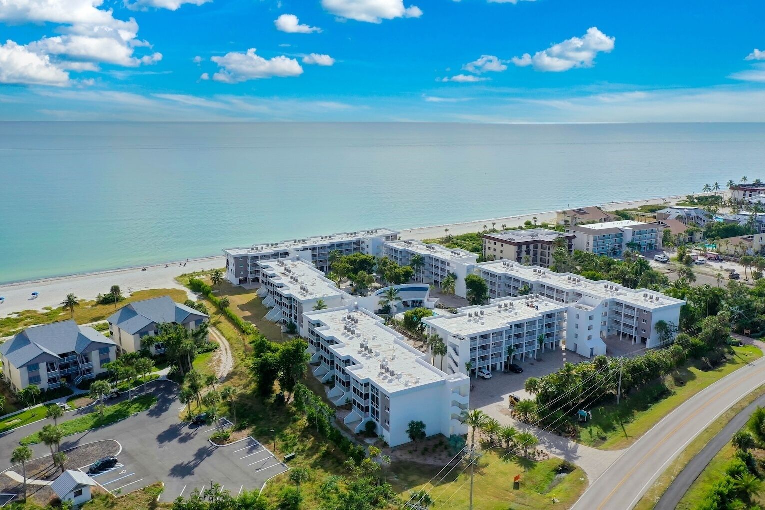 Un complexe hôtelier situé sur la côte, composé de plusieurs bâtiments, avec un parking et une plage en arrière-plan.