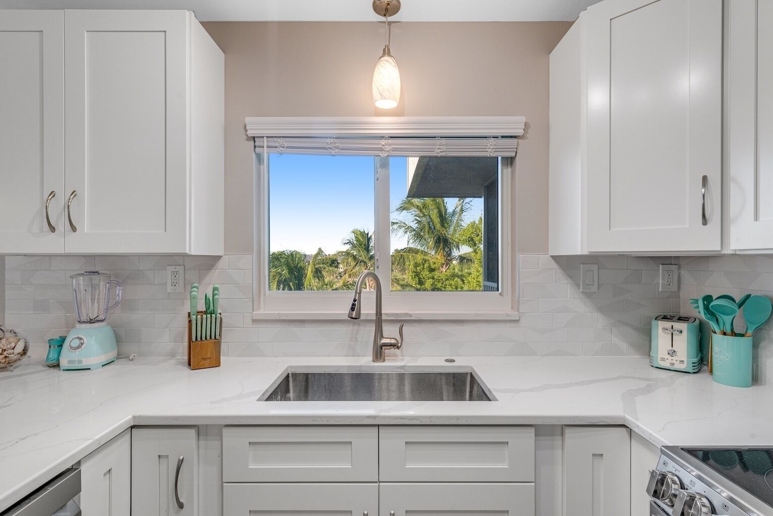 A kitchen with white cabinets, a window with a view of palm trees, a blender, and a toaster.