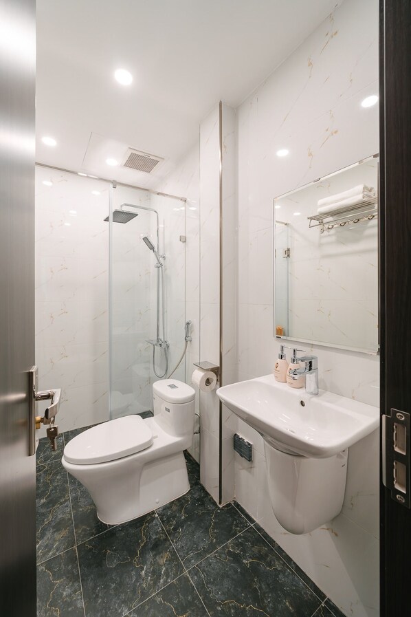 Un baño moderno con ducha de vidrio, inodoro blanco, lavamanos con espejo y suelo de mármol.
