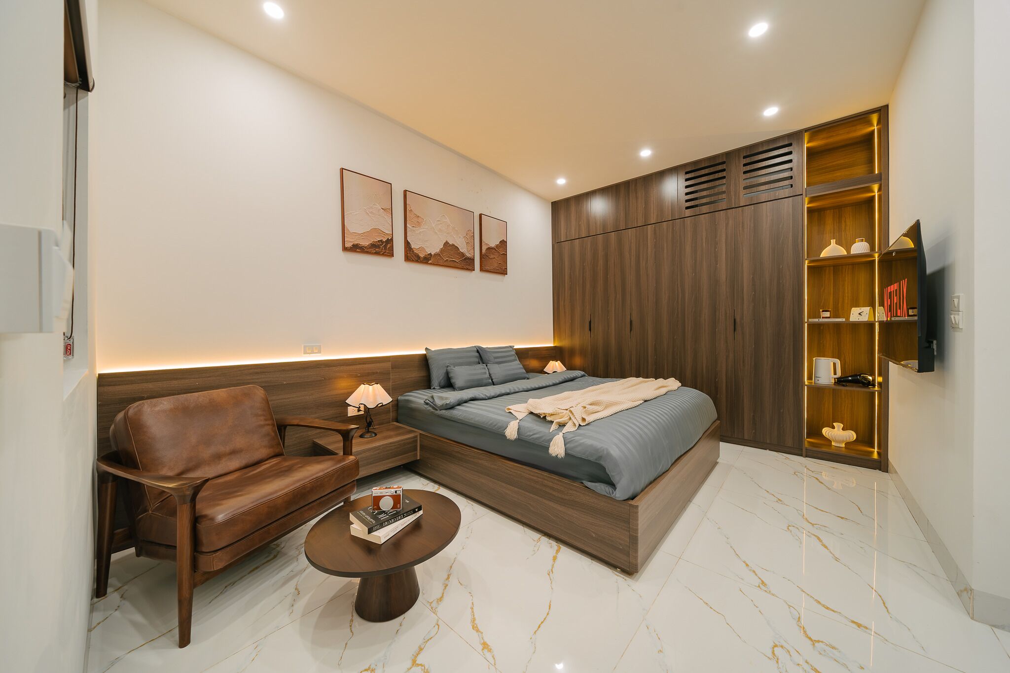 Quarto moderno com cama, sofá de couro, mesinha e estante para televisão.