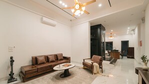 A modern living room with a brown leather sofa, a round coffee table, and a beige armchair. There is a ceiling fan, recessed lighting, and a marble floor. - Tamundi Embassy - Diplomatic Quarter - West Lake Hanoi (Hanoi)