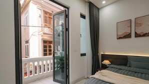 A bedroom with a bed, a nightstand, a lamp, and a view of a building through a glass door. - Tamundi Embassy - Diplomatic Quarter - West Lake Hanoi (Hanoi)