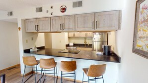 Une cuisine moderne dotée d’un îlot central, de tabourets de bar et d’un réfrigérateur en acier inoxydable.