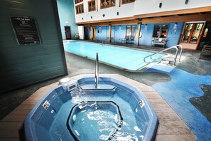 Uma banheira de hidromassagem com escada de metal, piscina com deck azul e um edifício com janelas amplas e parede externa azul.