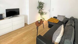 Un soggiorno moderno con un divano, una televisione, un armadietto bianco, un tavolino con una pianta e una scala.