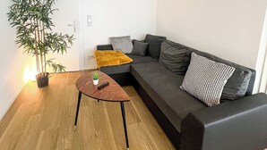 Un soggiorno moderno con un divano ad angolo grigio scuro, un tavolino in legno, una pianta in vaso e una lampada da tavolo.