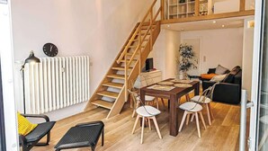Un appartamento moderno con una scala in legno, un'area pranzo con tavolo e sedie, un termosifone e un divano.