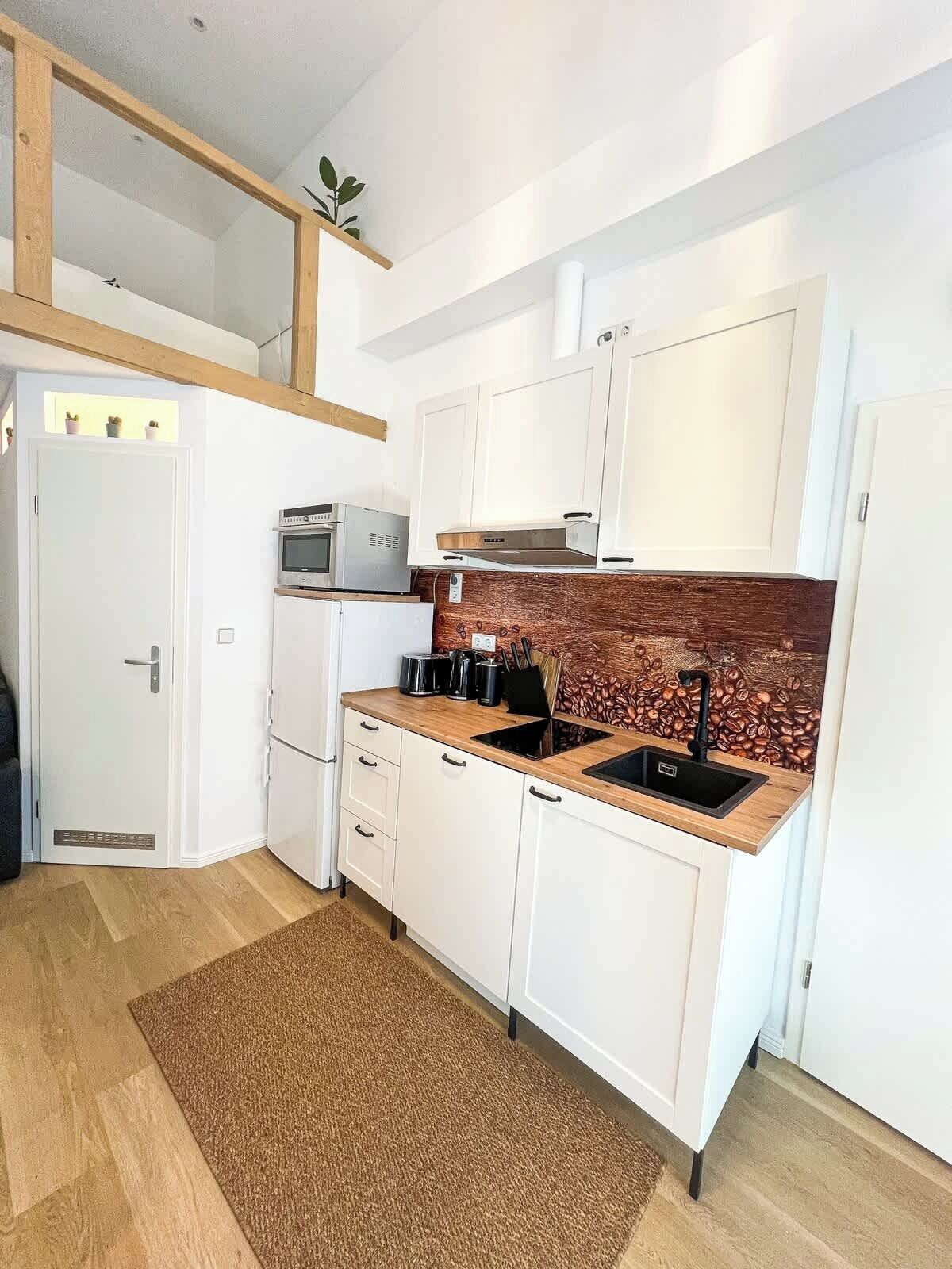A compact kitchen with white cabinets, a wooden countertop, a built-in oven, and a coffee-themed backsplash.