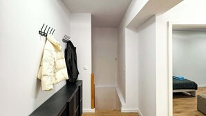 Ein Flur mit Kleiderhaken, einem schwarzen Konsolentisch und einem Bett im angrenzenden Zimmer.