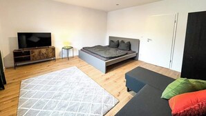 Ein modernes Schlafzimmer mit Bett, Fernseher, Sofa und einem kleinen Tisch.