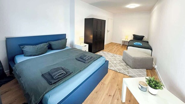 Ein modernes Schlafzimmer mit einem großen Bett, einer kleinen Couch, einem Schreibtisch und einem Kleiderschrank.