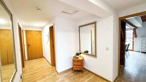 Un corridoio con pavimento in legno, una porta in legno, uno specchio, un piccolo tavolino con una pianta e un comò bianco.