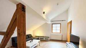 Un moderno loft con soffitto spiovente, un'ampia finestra, televisione integrata e un angolo salotto accogliente.