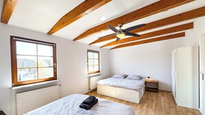 Una camera da letto con un letto, una ventola a soffitto, travi in legno, un termosifone e una finestra.