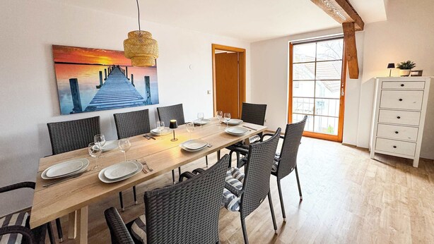 Zona pranzo con un tavolo di legno lungo, sedie in vimini e un quadro raffigurante un tramonto sulla parete.