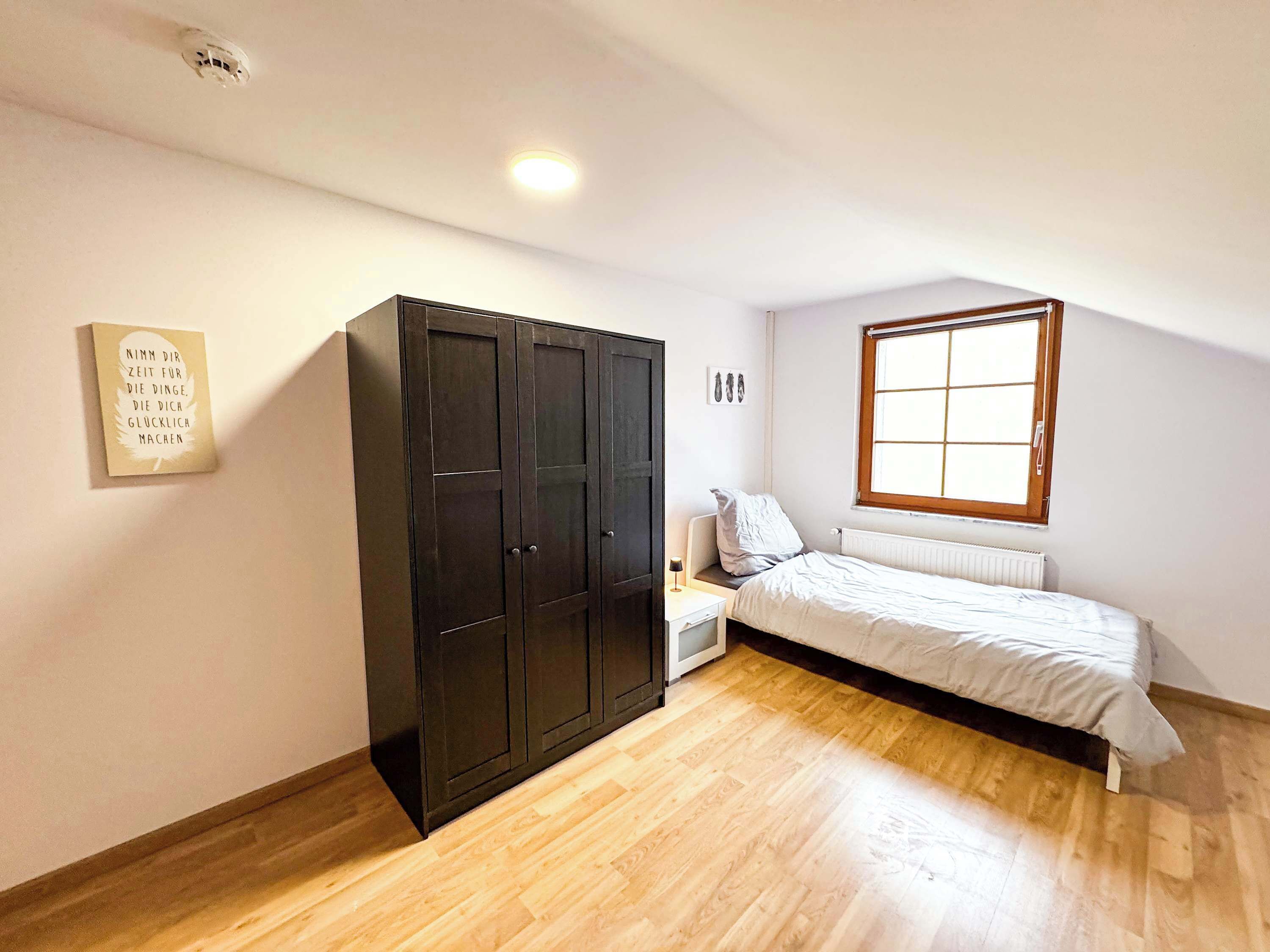 A bedroom with a bed, a wardrobe, a window, and a radiator.