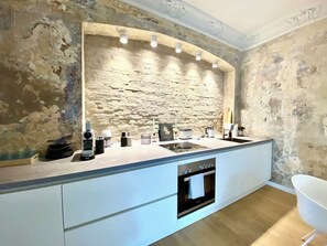 Eine moderne Küche mit einer Wand aus Stein, einem eingebauten Ofen und einem weißen Spülbecken.