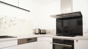Una cocina moderna con armarios blancos, horno empotrado, lavavajillas y cafetera.