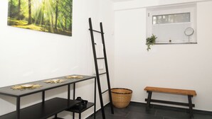 Una habitación con escritorio, banca, escalera, ventana con persianas y cesta.