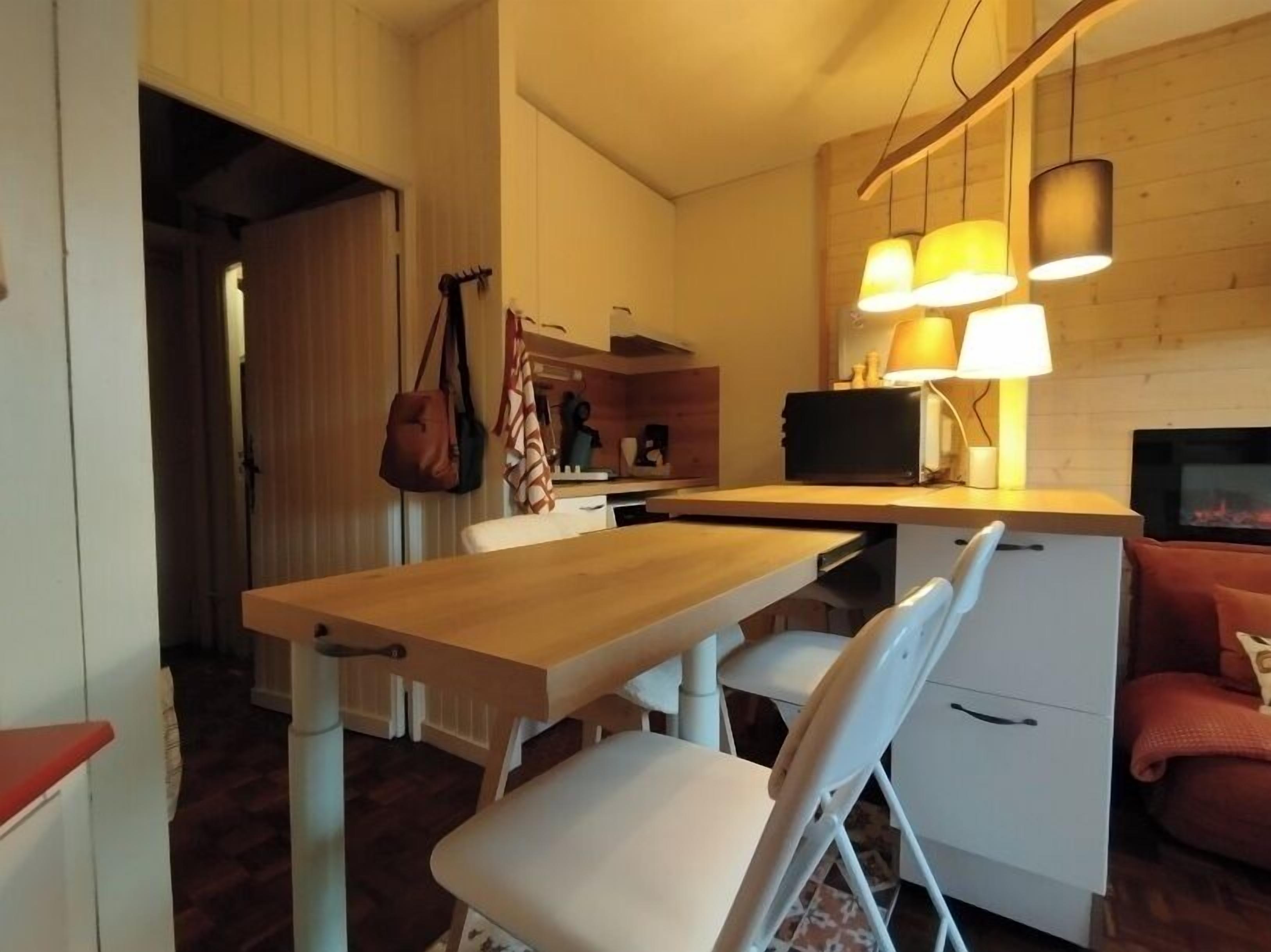 Une cuisine de taille réduite avec une table en bois, des chaises blanches et une cuisinière encastrée.