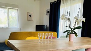 A dining area with a wooden table, five wine glasses, a potted orchid, and a yellow sofa. - La Maison Jaune - 4 bedrooms - sleeps 7 - Quiet location (Saint-Amand-sur-Fion)
