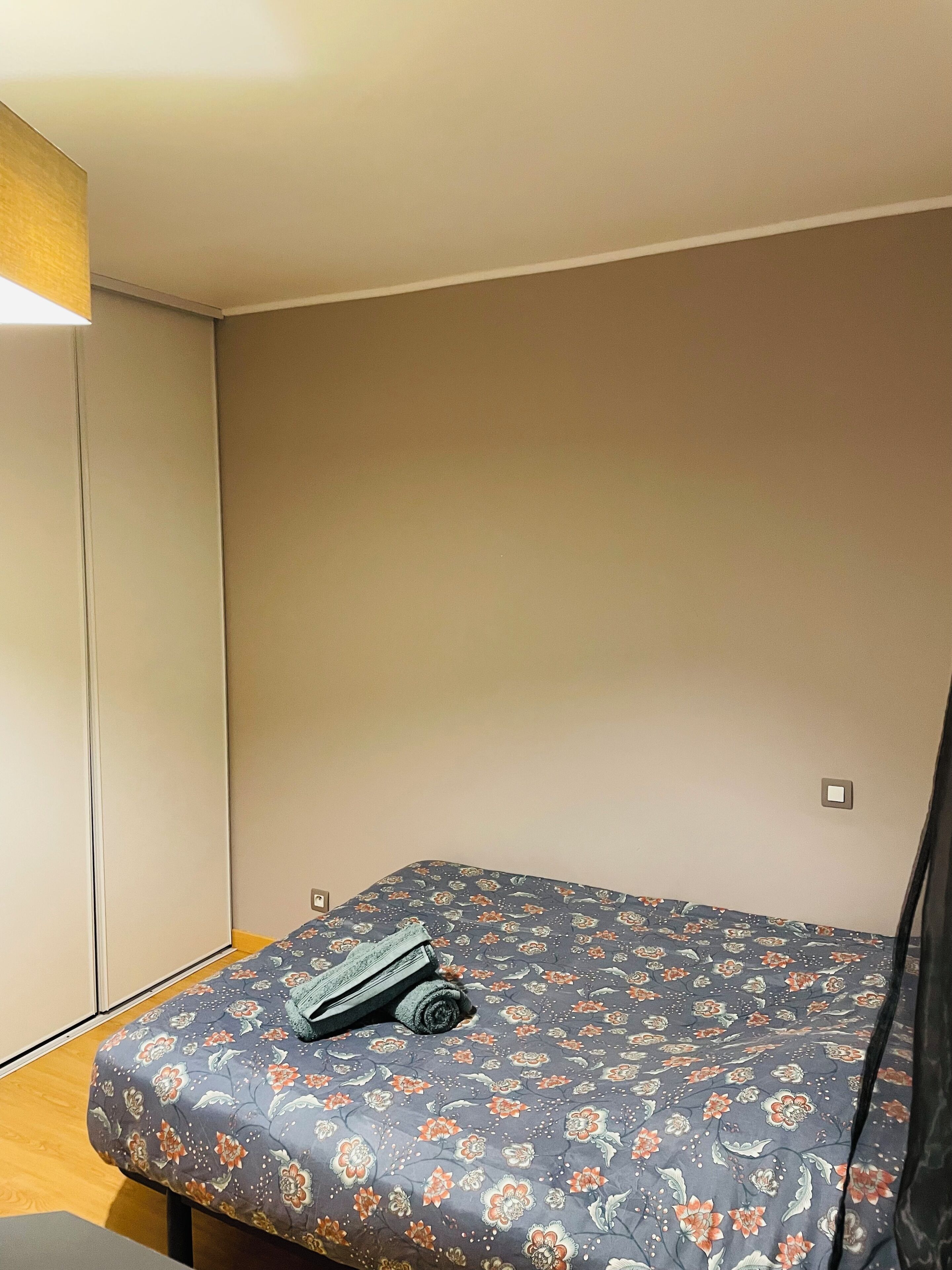 Ein kleiner, schlichter Raum mit einem Bett, einem Kleiderschrank und einer einzelnen Lampe.