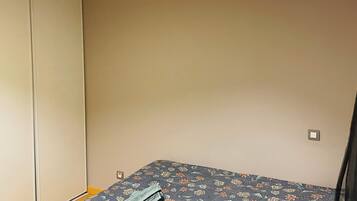 Ein kleiner, schlichter Raum mit einem Bett, einem Kleiderschrank und einer einzelnen Lampe.