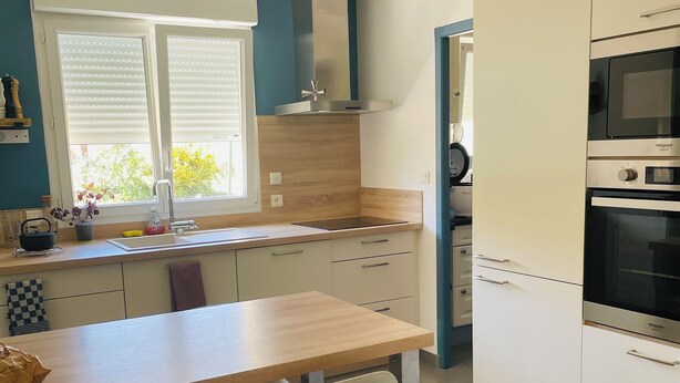 A modern kitchen with a wooden table and two chairs, a built-in oven, and a window with blinds. - La Maison Jaune - 4 bedrooms - sleeps 7 - Quiet location (Saint-Amand-sur-Fion)
