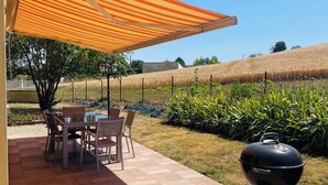 An outdoor patio with a tiled floor, a table with chairs, a barbecue grill, and a striped canopy. - La Maison Jaune - 4 bedrooms - sleeps 7 - Quiet location (Saint-Amand-sur-Fion)