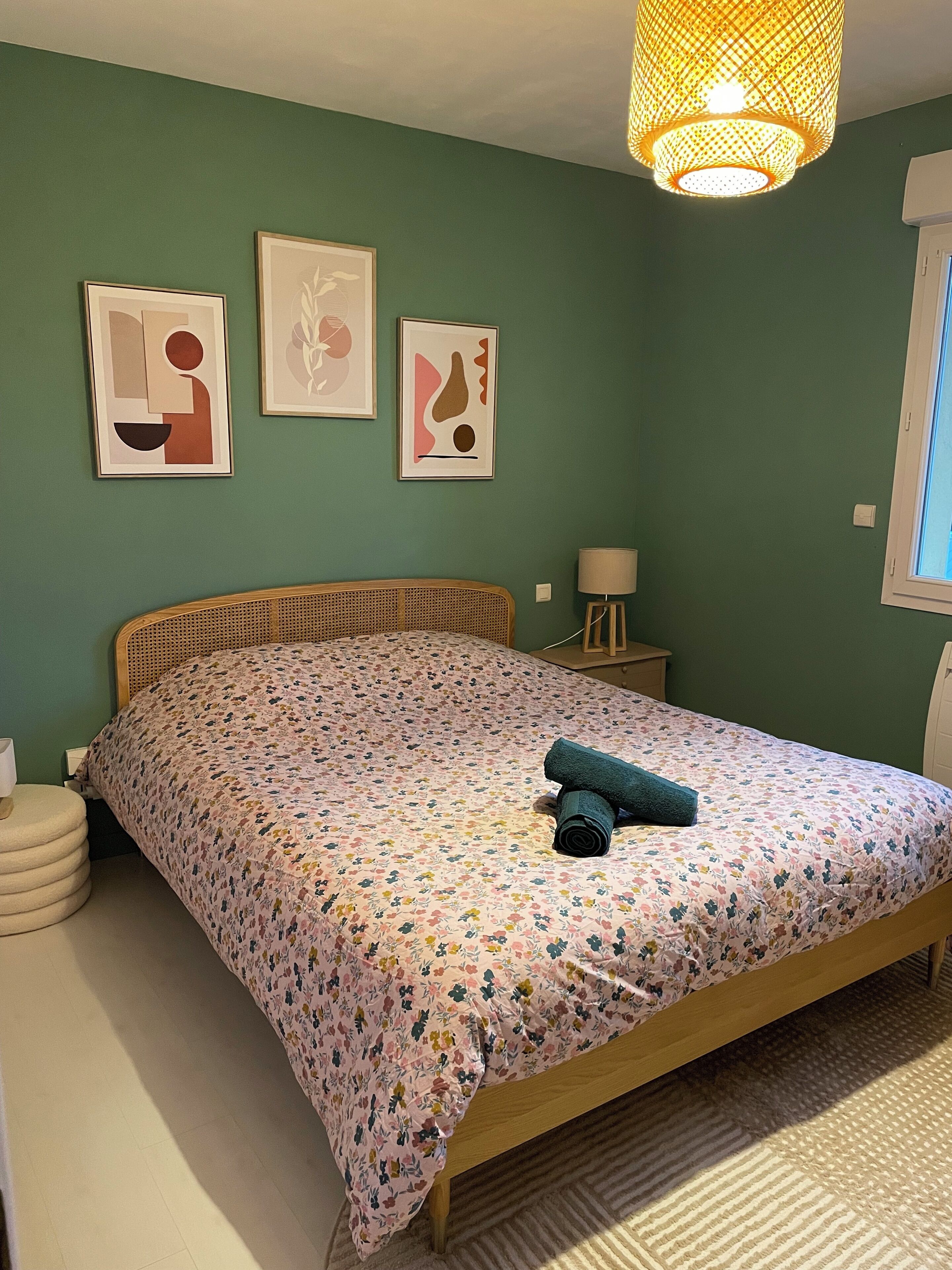 Quarto com colcha florida, cabeceira de madeira, mesa de cabeceira com abajur e três quadros na parede.