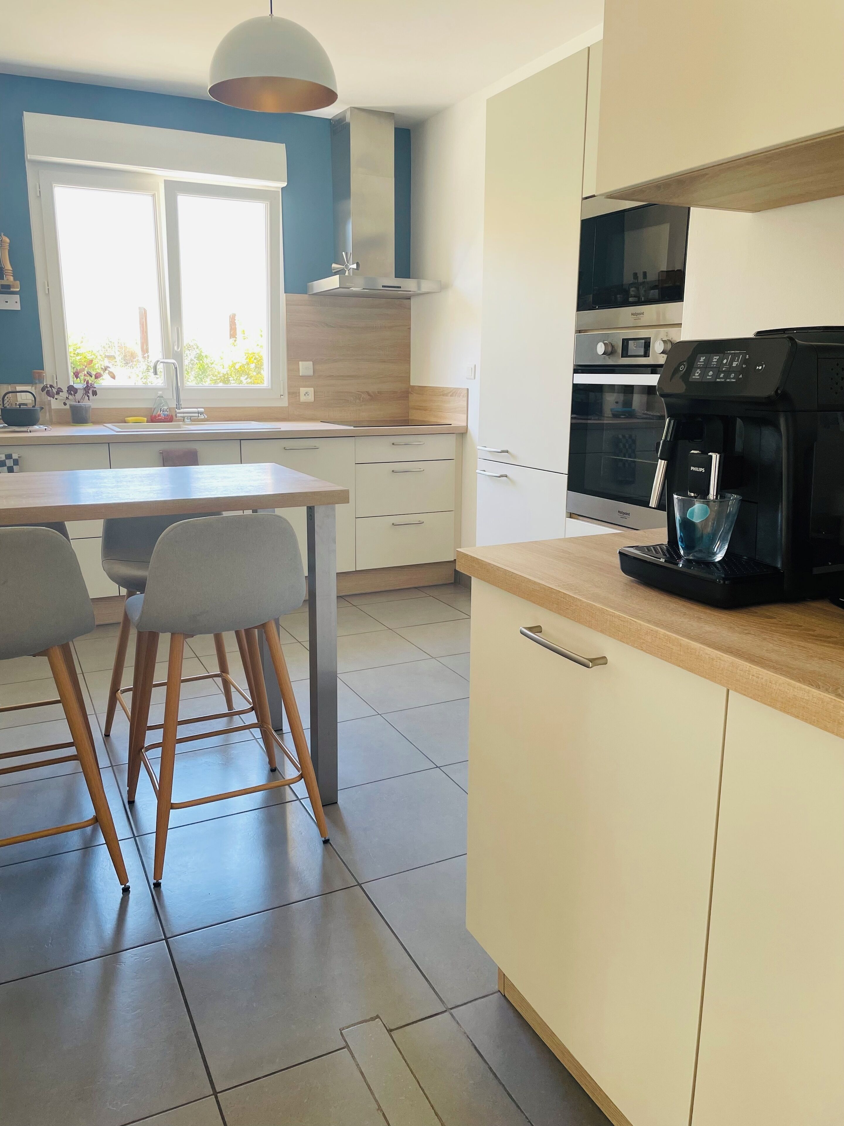 A modern kitchen with a built-in oven, a coffee machine, and a window with a view of greenery.
