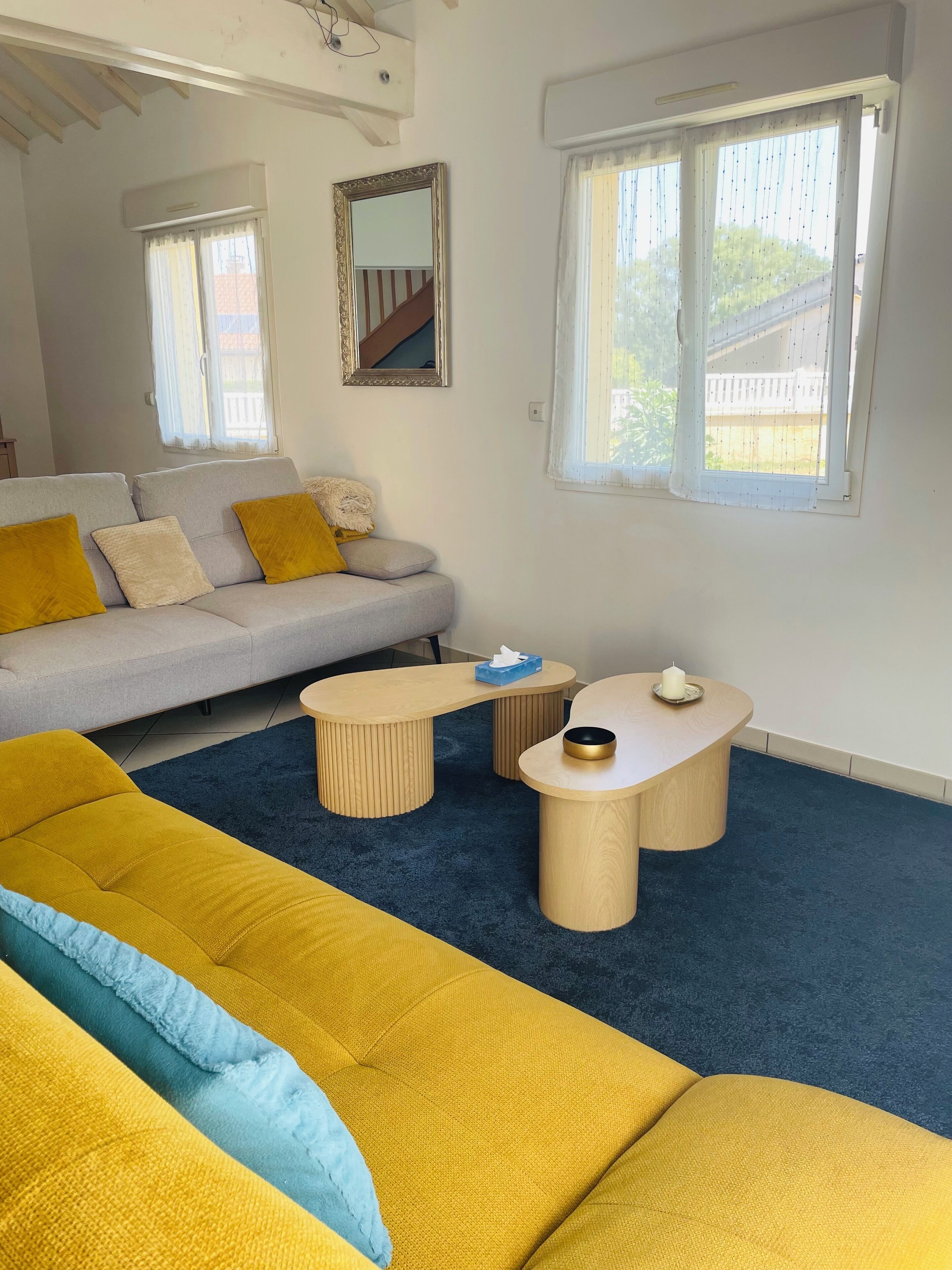 Ein modernes Wohnzimmer mit einer Couch, zwei Couchtischen und einem großen Fenster mit Vorhängen.