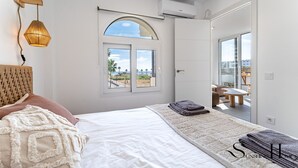 Un dormitorio con cama, ventana con vistas, lámpara colgante y puerta que da a un balcón.