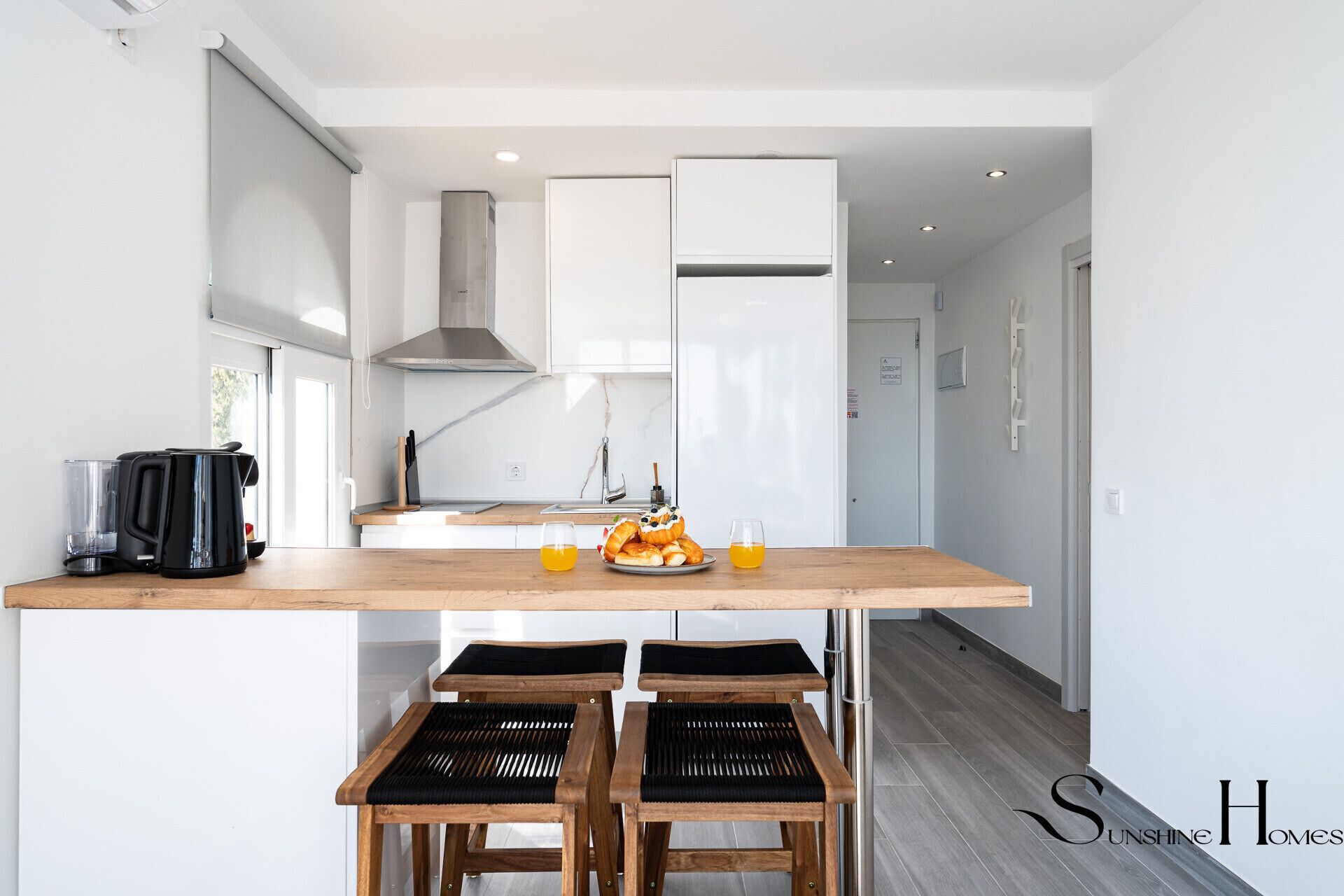 Een moderne keuken met witte kasten, een roestvrijstalen afzuigkap en een houten kookeiland met twee zwarte, beklede barkrukken.