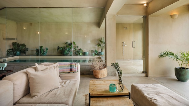 Ein modernes Wohnzimmer mit einem beigefarbenen Sofa, einem Holztisch und einem großen Panoramafenster mit Blick auf einen Swimmingpool.