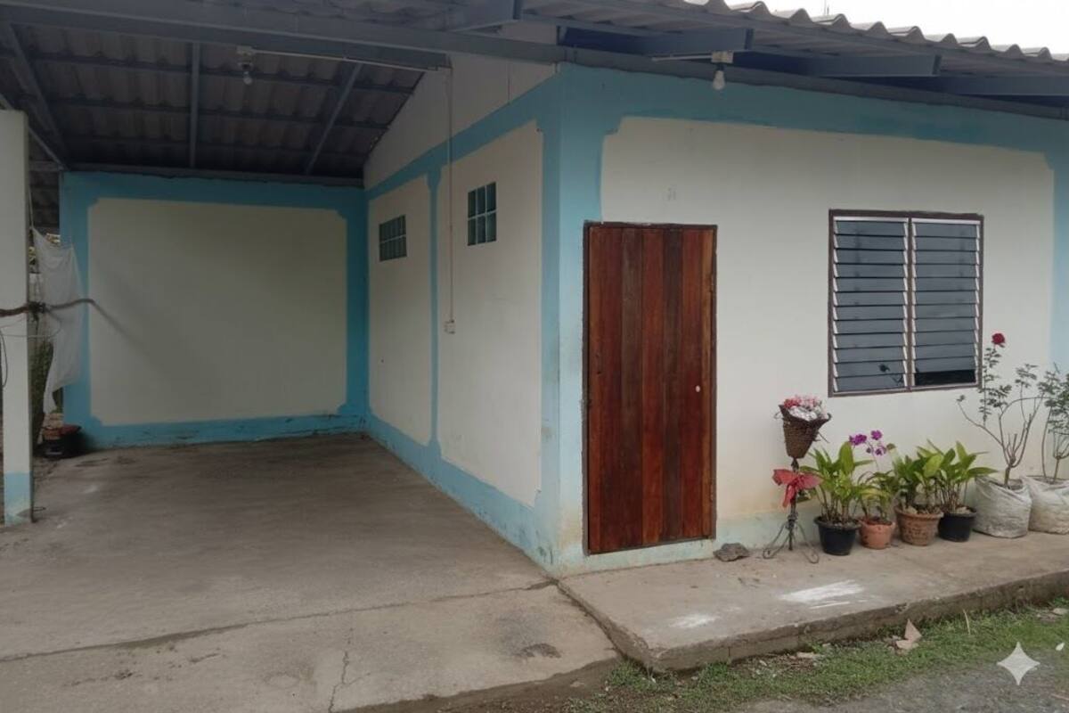 A single-story building with a blue and white exterior, a wooden door, and a window with horizontal bars. There are potted plants on the right side.